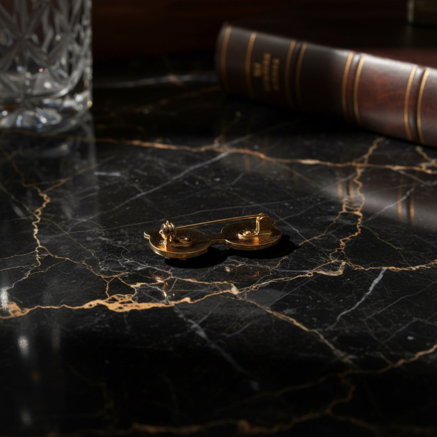 Gold scale brooch on a dark marble surface with a book and glass in the background