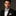 Man wearing a black suit with a patterned bow tie and pocket square on a dark background