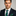 Man wearing a dark suit with a blue and green striped tie against a gray background