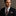 Man wearing a dark suit with a patterned tie and pocket square against a neutral background