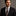 Man wearing a black suit with a patterned tie and pocket square on a gray background