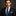 Man wearing a black suit with a blue patterned tie and white shirt against a dark background