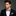 Man wearing a black suit with a red and white checkered bow tie and pocket square on a gray background