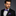 Man wearing a black suit with a purple bow tie and pocket square on a gray background