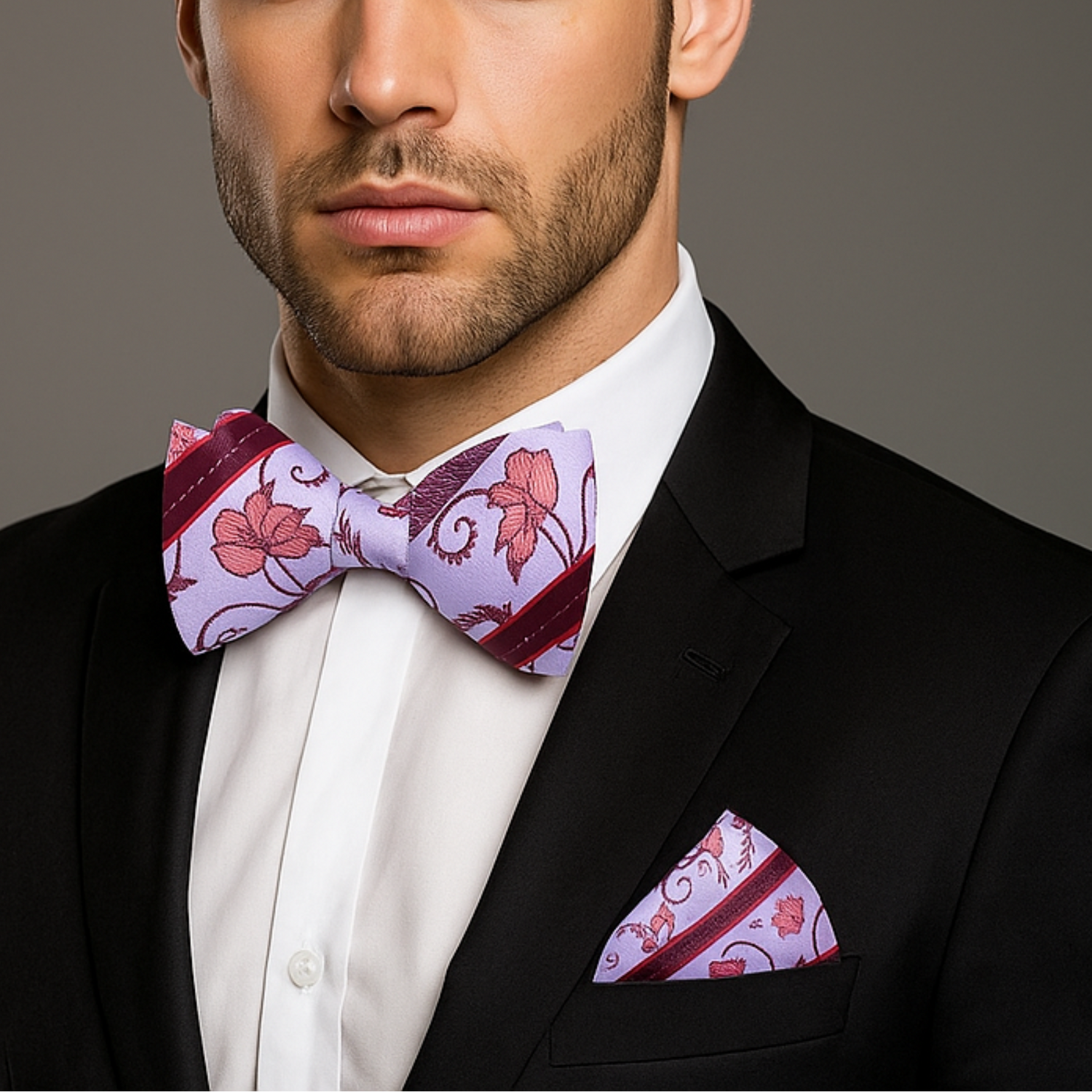 Man wearing a black suit with a purple bow tie and matching pocket square against a gray background