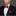 Man wearing a black suit with a red plaid bow tie and pocket square on a gray background