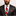 Man wearing a black suit with a red and white striped tie on a light background
