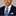 Man wearing a dark suit with a blue patterned tie and pocket square on a gray background