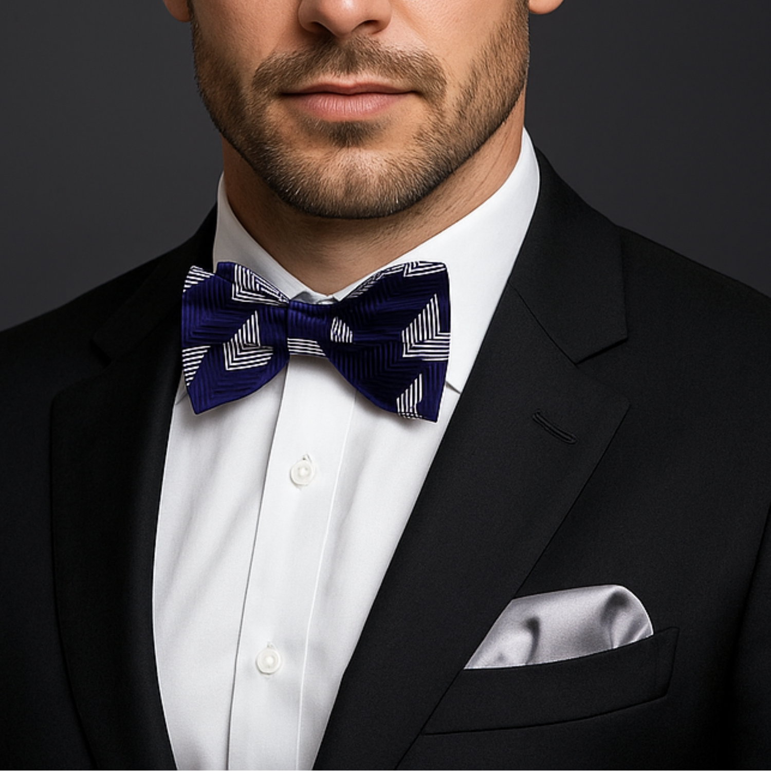 Man wearing a black suit with a white shirt and patterned bow tie on a dark background
