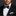 Man wearing a black suit with a white shirt and patterned bow tie on a dark background