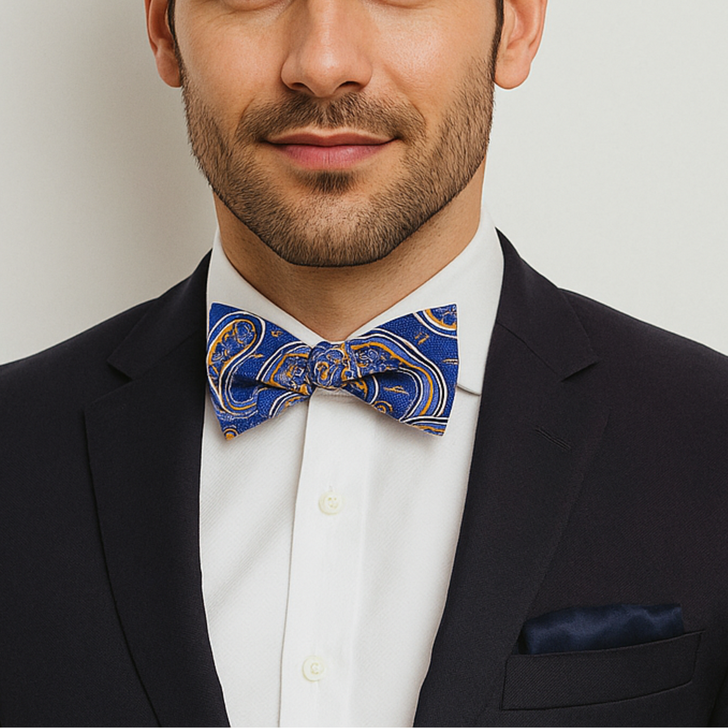 Man wearing a black suit with a white shirt and blue and yellow paisley patterned bow tie on a light gray background