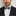Man wearing a black suit with a white shirt and blue and yellow paisley patterned bow tie on a light gray background