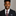 Man wearing a black suit with a red patterned tie against a gray background
