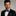Man wearing a black suit with a blue checkered bow tie and pocket square on a gray background
