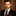 Man wearing a black suit with a patterned tie against a brown background
