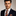 Man wearing a dark suit with an orange and gray striped tie against a neutral background