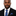 Man wearing a black suit with a blue and gray striped tie and pocket square on a white background