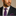 Man wearing a dark suit with a blue tie and pocket square featuring red patterns on a beige background