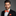 Man wearing a black suit with an orange bow tie and pocket square on a gray background
