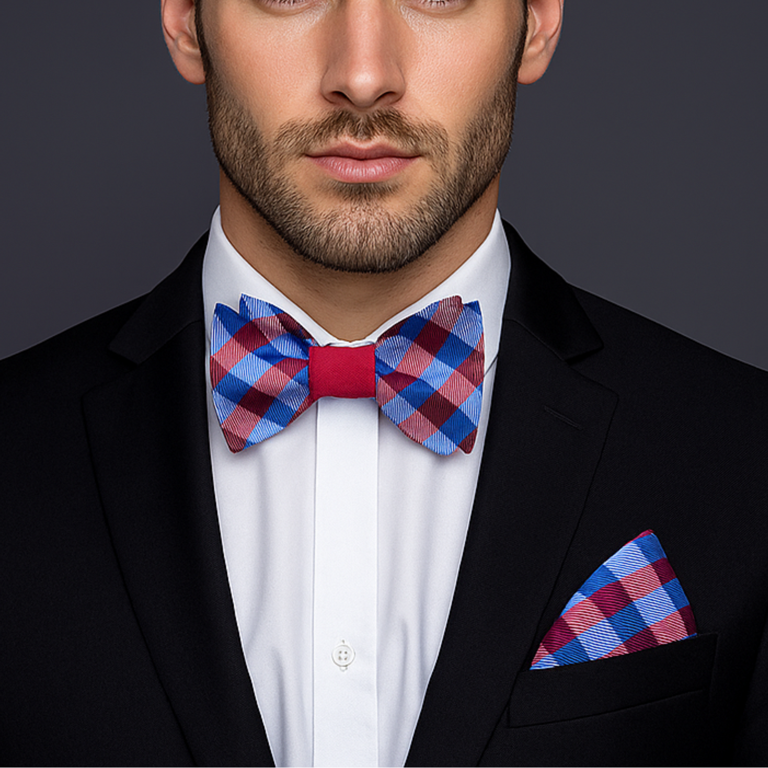 Man wearing a black suit with a red and blue checkered bow tie and pocket square on a dark background