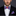 Man wearing a black suit with a red and blue checkered bow tie and pocket square on a dark background