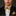 Man wearing a black suit with a yellow and blue bow tie and pocket square on a dark background