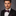 Man wearing a black suit with a red polka dot bow tie against a gray background
