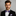 Man wearing a black suit with a purple plaid bow tie and pocket square against a gray background