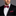 Man wearing a black suit with a burgundy and white polka dot bow tie and pocket square on a gray background