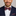 Man wearing a navy suit with a red, white, and blue striped bow tie and pocket square on a gray background