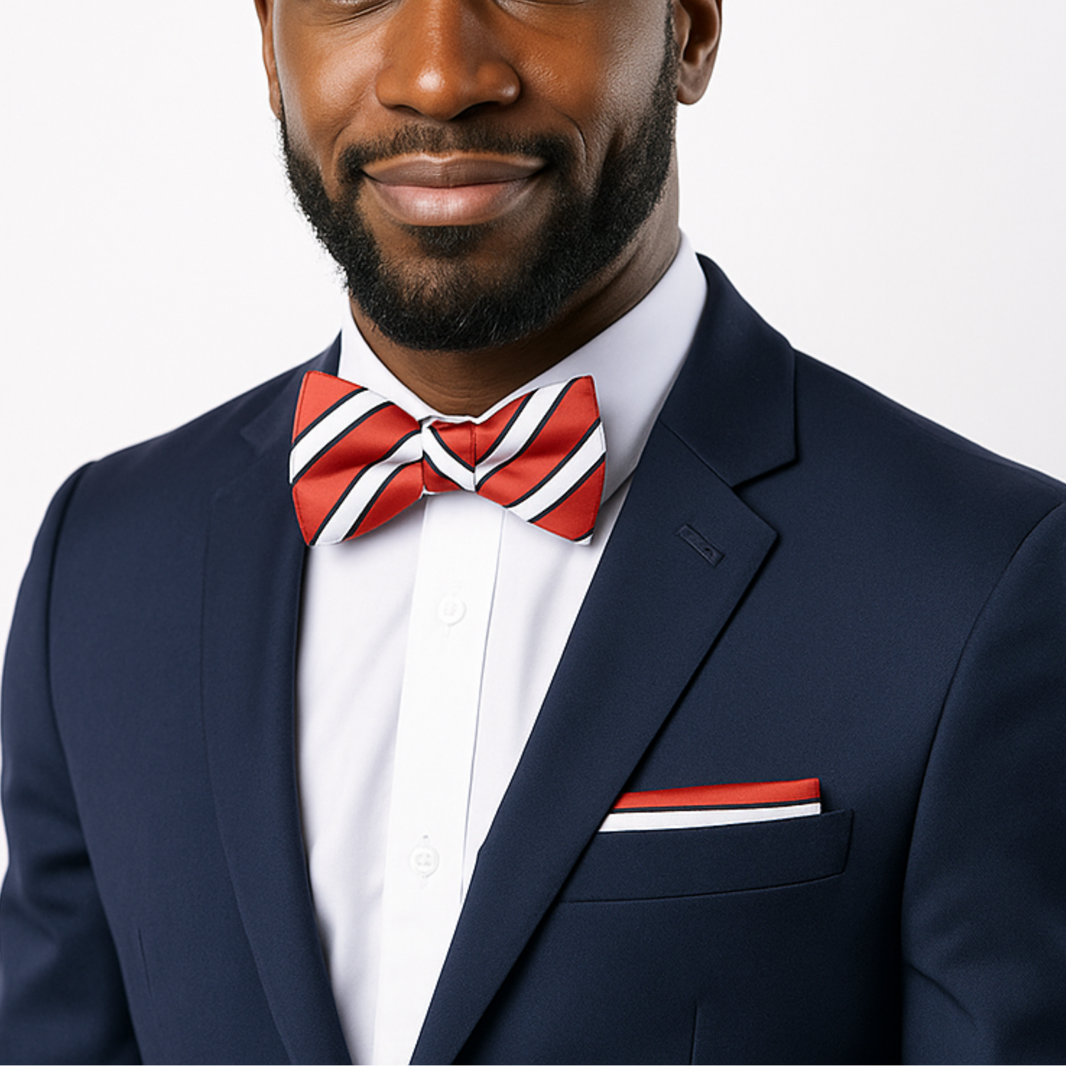 Man wearing a navy suit with a red and white bow tie on a light gray background