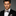 Man wearing a black suit with a patterned blue and brown paisley bow tie and pocket square on a gray background