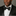 Man wearing a black tuxedo with a black and white floral bow tie against a gray background