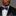 Man wearing a black suit with a purple floral bow tie and pocket square on a gray background