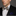 Man wearing a black suit with a patterned brown floral and stripe bow tie and accenting blue and brown pocket square on a gray background
