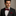 Man wearing a black suit with a white shirt and red bow tie and pocket square against a neutral background