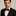 Man wearing a black suit with a white shirt and red bow tie and pocket square against a neutral background 2