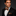 Man wearing a black suit with an orange and blue stripe bow tie and pocket square on a dark background