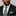 Man wearing a black suit with a striped tie and pocket square on a plain background