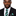Man wearing a black suit with a green and brown striped tie and matching pocket square on a white background
