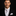 Man wearing a black suit with a white shirt, silver and pink geometric patterned tie, and pocket square on a dark background