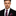 Man wearing a black suit with a red and blue striped tie and pocket square on a white background
