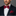 Man wearing a dark suit with a red and light grey polka geometric bow tie and pocket square on a gray background
