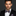 Man wearing a black suit with a purple striped bow tie against a dark background