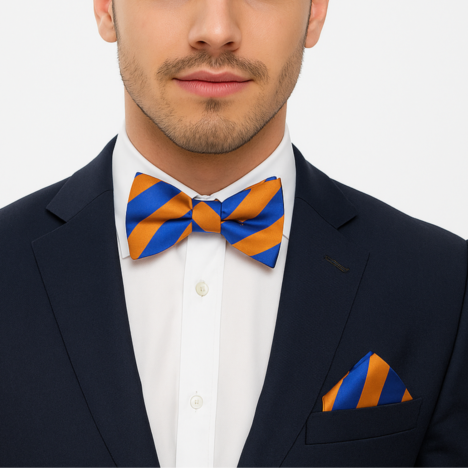 Man wearing a navy suit with an orange and blue stripe bow tie and pocket square on a white background