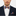 Man wearing a navy suit with an orange and blue stripe bow tie and pocket square on a white background