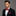 Man wearing a black suit with a red bow tie and pocket square on a gray background