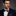 Man wearing a black suit with a blue and brown bow tie and accenting blue and brown geometric pocket square on a gray background