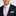 Man wearing a black suit with a pink and blue checkered tie and accenting blue pocket square.