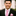 Man wearing a black suit with a pink polka with light blue dot tie and pocket square, smiling outdoors.